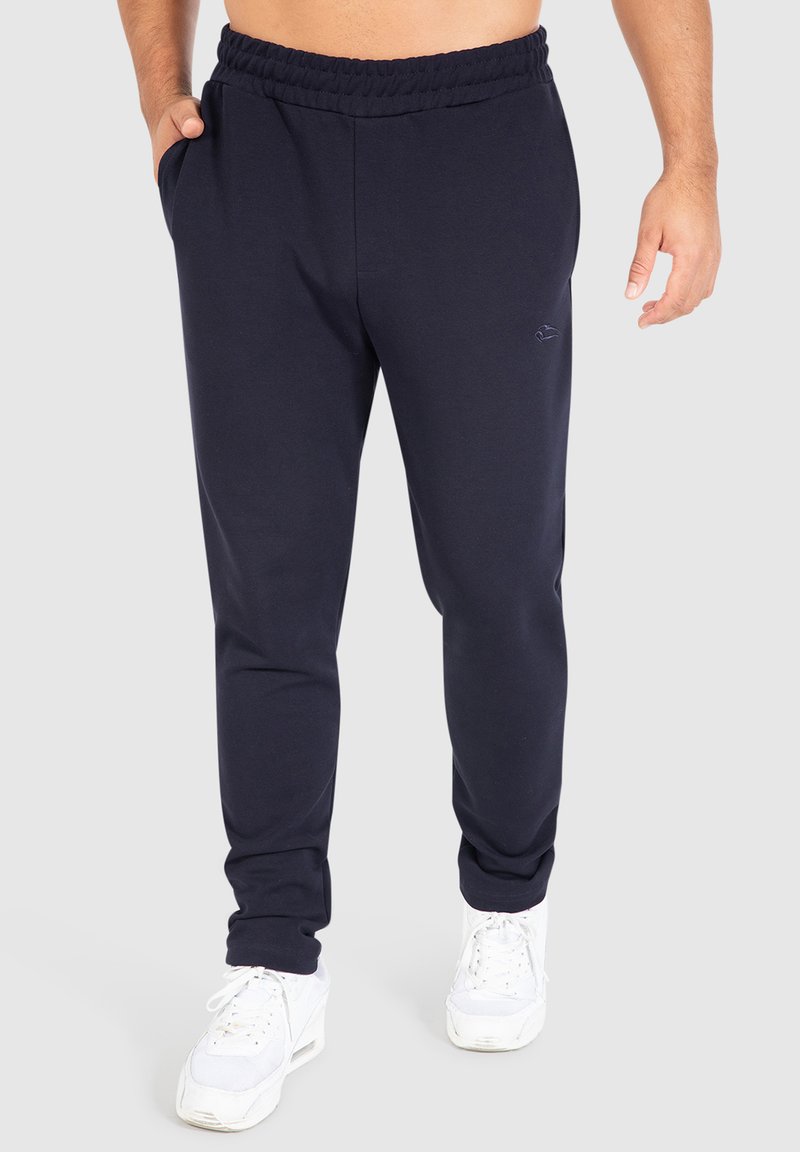 Pantalones de chándal azul marino fabricados con un tejido suave, con cintura elástica, bolsillos laterales y un pequeño logotipo en el muslo izquierdo.