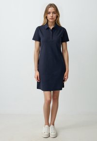 Marineblauwe polojurk van zachte katoen, korte mouwen, drie-knopen sluiting, knielengte, heeft een relaxte pasvorm en zijsplitten voor gemakkelijke beweging.
