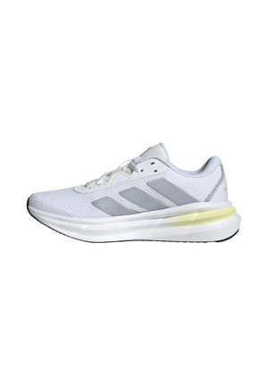 Zapatilla deportiva blanca con parte superior de malla y acentos grises. Presenta una suela acolchada con un detalle sutil en amarillo y una suela exterior de goma negra.