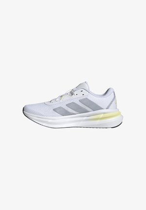 Zapatilla deportiva blanca con parte superior de malla y acentos grises. Presenta una suela acolchada con un detalle sutil en amarillo y una suela exterior de goma negra.