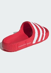 Red slip-on sandal with textured rubber material, white three-stripe design on the upper, and branded accent on the side.