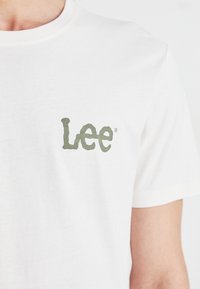 Hvit bomulls t-skjorte med en grønn stilisert "Lee" logo på forsiden. Klassisk crew neck-design med korte ermer.