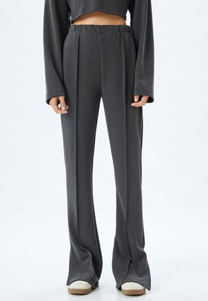 Pantalones de talle alto en gris oscuro, hechos de una tela suave con un diseño acampanado y una cinturilla elástica, que cuentan con pliegues frontales y costuras mínimas.