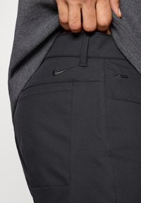 Μαύρο αθλητικό παντελόνι με λεία υφή, που διαθέτει μικρό μαύρο λογότυπο Nike, πολλαπλές τσέπες και εφαρμοστή ζώνη μέ σης.