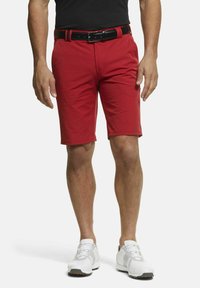 Shorts rouges avec une texture lisse, un design ajusté et une coupe droite, accompagnés d'une ceinture noire. Portés avec des chaussures de sport blanches.