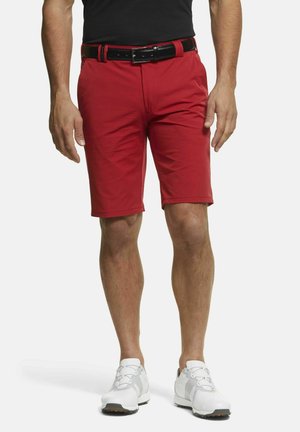 Rote Shorts mit glatter Textur, figurbetontem Design und geradem Schnitt, kombiniert mit einem schwarzen Gürtel. Getragen mit weißen Sportschuhen.