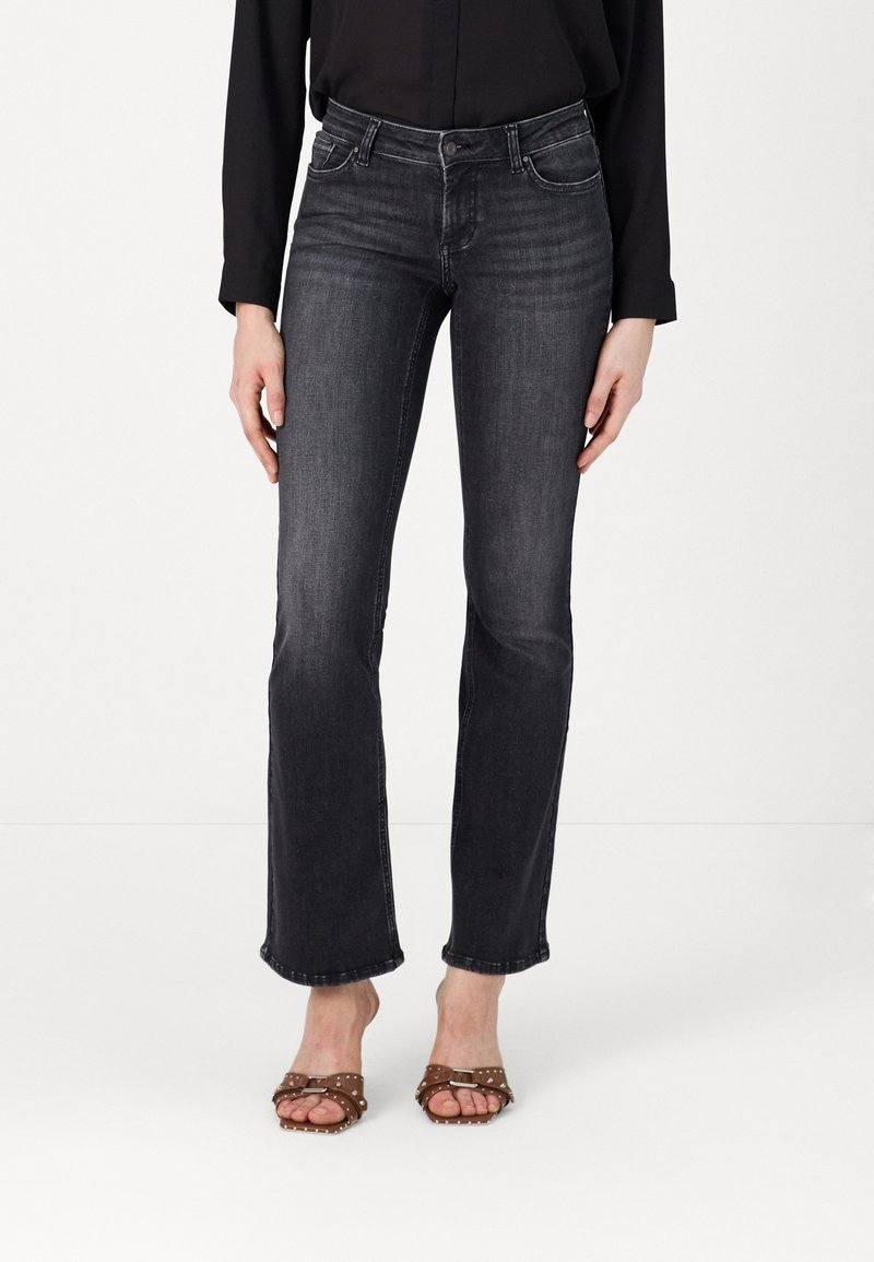 Jean flare en denim noir avec taille mi-haute, décoloration subtile et design à cinq poches. Assorti à des sandales à talons cloutées brunes.