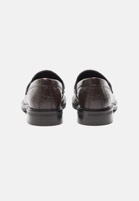 Tummanruskeat loaferit, joissa on krokotiilinkuositekstuuria, pyöreä kärki ja sileä musta pohja. Avoin takakappale helppoa pukemista varten.