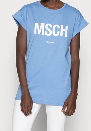 Person wearing a light blue T-shirt with "MSCH" and "EST MMX" printed in white, paired with white pants, plain background.