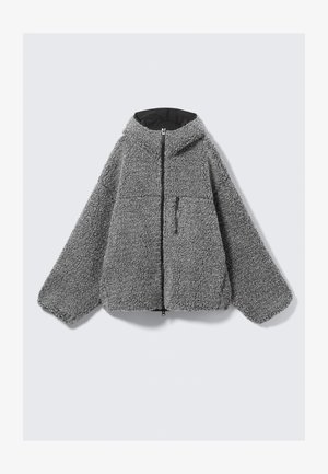 Szara polarowa kurtka z kapturem, z zamkiem błyskawicznym, elastycznymi mankietami i jedną kieszenią na klatce piersiowej. Charakteryzuje się miękką, teksturowaną powierzchnią oraz prostym, luźnym krojem.