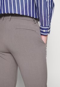 Grå byxor med en slät yta och en slim fit. Har en bakficka och är kombinerade med en blå randig skjorta.