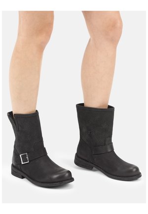 Nogi w czarnych skórzanych butach sięgających do połowy łydki, z teksturowaną cholewką, bocznym zamkiem błyskawicznym i ozdobną klamrą na białym tle.