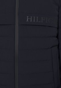 Granatowa pikowana kurtka puchowa z przeszyciami, zamkiem błyskawicznym z przodu oraz nadrukowanym logo na klatce piersiowej. Wykonana z lekkiego materiału.