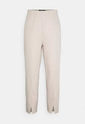 Pantalon beige taille haute fuselé avec détails des coutures avant et petites fentes à l’avant de l'ourlet.