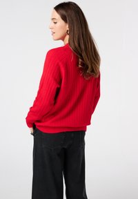 Rode geribbelde trui met een losse pasvorm, ronde halslijn en verlaagde schouders, gecombineerd met hoog-waist zwarte wijde broek.