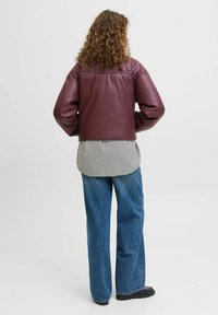 Bordowa, krótka skórzana kurtka z bufiastymi rękawami, w zestawieniu z koszulą w kratę i niebieskimi dżinsami o szerokich nogawkach, noszona z czarnym obuwiem.