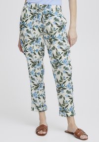 Blommiga byxor med krämfärgad botten och mönster av blå och gröna blommor. Elastiskt midjeband med dragsko. kanten är något uppvikt, matchat med bruna sandaler.