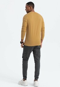 Langärmliges, senfgelbes Shirt kombiniert mit grauen Cargo-Hosen. Das Shirt hat einen figurbetonten Schnitt; die Hose verfügt über Seitentaschen und schmal zulaufende Beine.