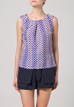 Haut sans manches en tissu crème avec un motif en chevrons bleu, doté d'un décolleté plissé et d'une coupe décontractée, associé à un short sombre.