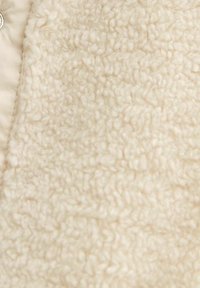 Cream-colored soft fleece fabric with a looped, textured surface and stitched edge visible on the left side.