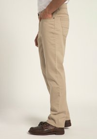 Chinos de algodón beige con bolsillos laterales y un bolsillo trasero, con un corte recto. Llevados con zapatos de cuero marrón.