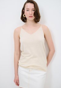 Beige top med V-udskæring og tynde stropper, lavet af blødt stof, parret med en hvid denimnederdel med frynset kant og dekorativ syning.