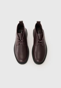 Scarpe in pelle borgogna con finitura liscia, punta rotonda, design con lacci e suola in gomma nera contrastante. Linee pulite e dettagli minimi.