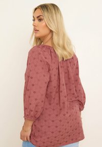 Rosafärgad blus med trekvartslånga ärmar, med blommönster och en texturerad tyg. Halsringningen är rynkad för en lös passform.