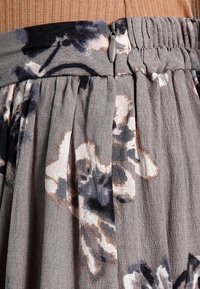 Jupe plissée à motif floral en gris avec des touches de bleu marine et de beige, munie d'une taille élastique et d'une fermeture éclair discrète.