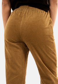 Pantalons en velours côtelé d'une couleur marron chaud, présentant un motif côtelé texturé, une taille élastique et une coupe décontractée.