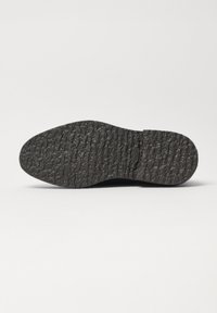 Černá gumová podrážka obuvi s texturovaným, vzorovaným povrchem, která má drážky a výstupky pro lepší přilnavost a trakci.