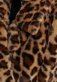 CAPPOTTO IN FINTA PELO A MACCHIE DI LEOPARDO con una texture morbida, macchie marroni e nere e un design con colletto. Chiusura con zip visibile sul lato sinistro.