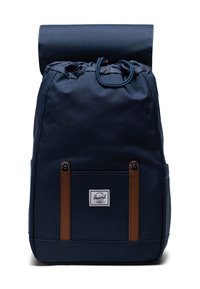 Mochila de tela azul marino con cierre de tipo roll-top, correas de cuero marrón, un bolsillo frontal y un parche con logo en la base. Textura suave.