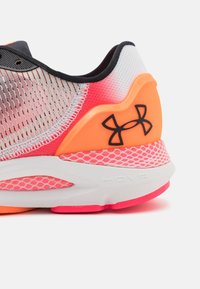 Chaussure de sport avec une tige en mesh de dégradé rose, des accents orange, un logo noir, et une semelle intermédiaire blanche texturée avec un motif hexagonal.
