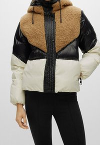 Giubbotto imbottito con parte superiore in pile marrone, maniche nere lucide e parte inferiore crema. Presenta un cappuccio e chiusura con zip, oltre a due tasche laterali.