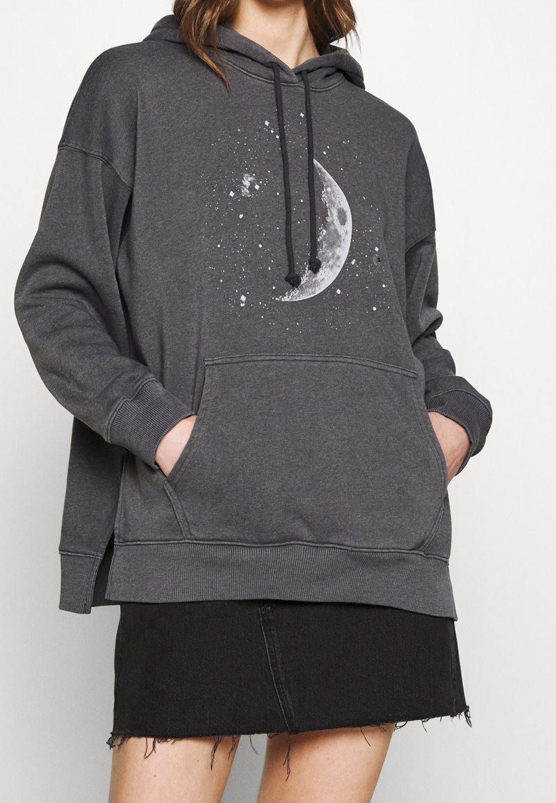 Sweat à capuche gris avec une poche avant, arborant un motif de lune et d'étoile. Fini avec une capuche à cordon de serrage et des poignets et ourlet côtelés.
