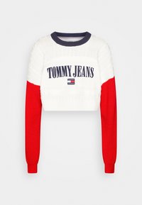 Pull court avec des manches rouges, un corps blanc et des accents navy. Présente le logo "TOMMY JEANS" en navy sur la poitrine. Design en tricot texturé.