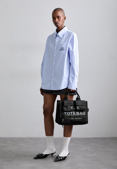 Light blue striped shirt, black tote bag with text, denim skirt, white ankle socks, and black pointed-toe heels.
