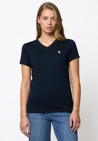 Marine V-hals T-skjorte laget av mykt stoff, med korte ermer og en liten logo på venstre bryst. Kombinert med blå jeans.