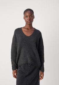 Dunkelgrauer V-Ausschnitt-Pullover mit langen Ärmeln, weichem Material und leicht abgerundetem Saum, kombiniert mit einem dunkelgrauen Rock. Keine sichtbaren Muster.