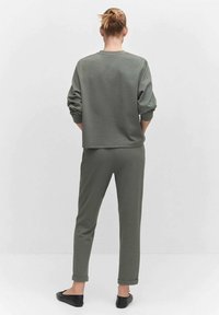Olivgrüner Sweatshirt und passende Jogginghose aus weichem Stoff, mit umgeschlagenen Ärmeln und Bündchen, kombiniert mit schwarzen flachen Schuhen.