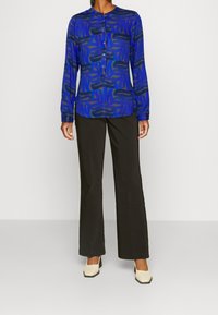 Blue long-sleeve shirt with abstract black pattern, button placket, paired with black wide-leg trousers and cream square-toe heels.
