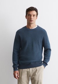 Marineblauer Rippstrickpullover mit Rundhalsausschnitt und langen Ärmeln, der einen kontrastierenden Rippbund und -manschetten aufweist.
