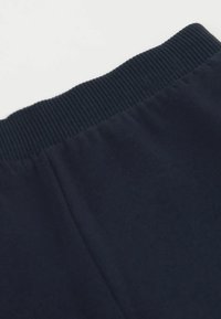 Zblízka pohled na pas neznačkové modré látky s žebrovaným elastickým lemem na čistém bílém pozadí.