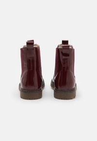 Bottines en cuir verni bordeaux avec un panneau arrière texturé, semelle en caoutchouc marron et languettes pour un enfilage facile. Doublées en fausse fourrure.
