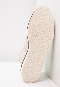 Białe trampki z teksturowaną gumową podeszwą i miękkim materiałem wierzchnim. Zaokrąglony kształt, minimalistyczny design, zawiera małą oznakowanie rozmiaru na podeszwie.