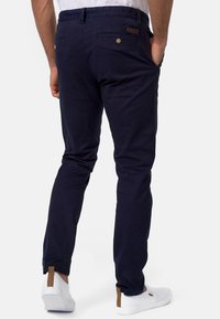 Navy cotton trousers with a slim fit, featuring back pockets, button accents, and a soft texture. Paired with white slip-on shoes.