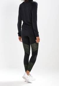 Czarna bluzka z długim rękawem połączona z legginsami w zielone paski w tygrysie. Gładki materiał, dopasowany krój i długość do kostek.