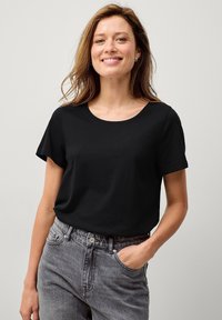 Schwarzes, kurzärmliges T-Shirt mit Rundhalsausschnitt, aus weichem Stoff. Kombiniert mit grauen, hochgeschnittenen Jeans im lässigen Schnitt.