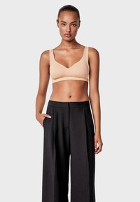 Sostén inalámbrico beige con tirantes anchos y acabado suave, combinado con pantalones negros de cintura alta con frente plisado y bolsillos laterales.